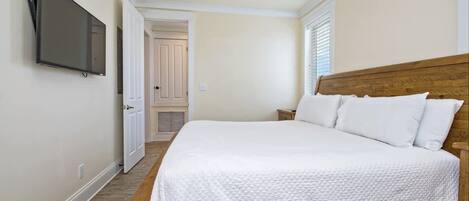 Un dormitorio con una cama, un ventilador de techo, un televisor montado en la pared y una puerta que da a otra habitación.