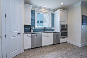 Uma cozinha moderna com armários brancos, painel de parede azul, eletrodomésticos de aço inoxidável e uma janela com vista.