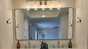 A bathroom with a large mirror, two sinks, and a vanity with drawers and a shelf.