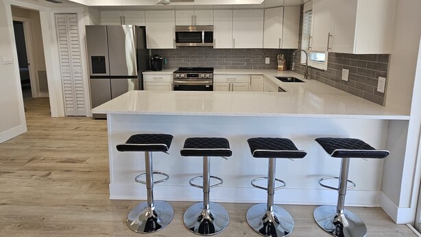 A modern kitchen with a central island, stainless steel appliances, and three black bar stools.
