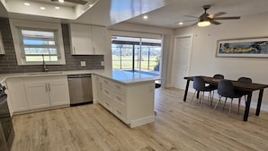 A modern kitchen with white cabinets, a dishwasher, and a dining area with a table and chairs.