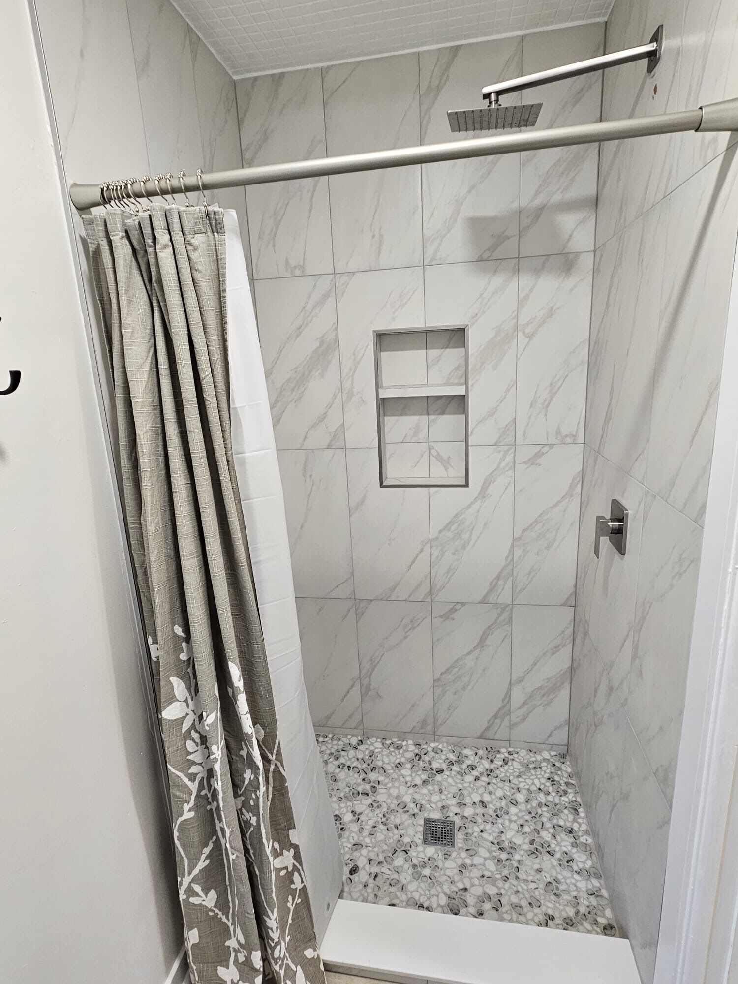 A shower with a glass door, marble tiles, and a showerhead.