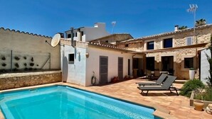 A swimming pool with lounge chairs, a stone wall, and a building with a tiled roof.