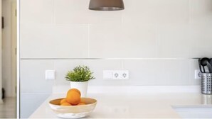 A modern kitchen with white tiles, a pendant light, a bowl of fruit, a potted plant, and a knife holder. - Villas2meet Casa Blanca Porto Cristo (Porto Cristo)