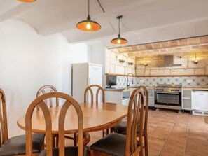 A dining area with a wooden table and chairs, a kitchen with a stone backsplash, and pendant lighting.