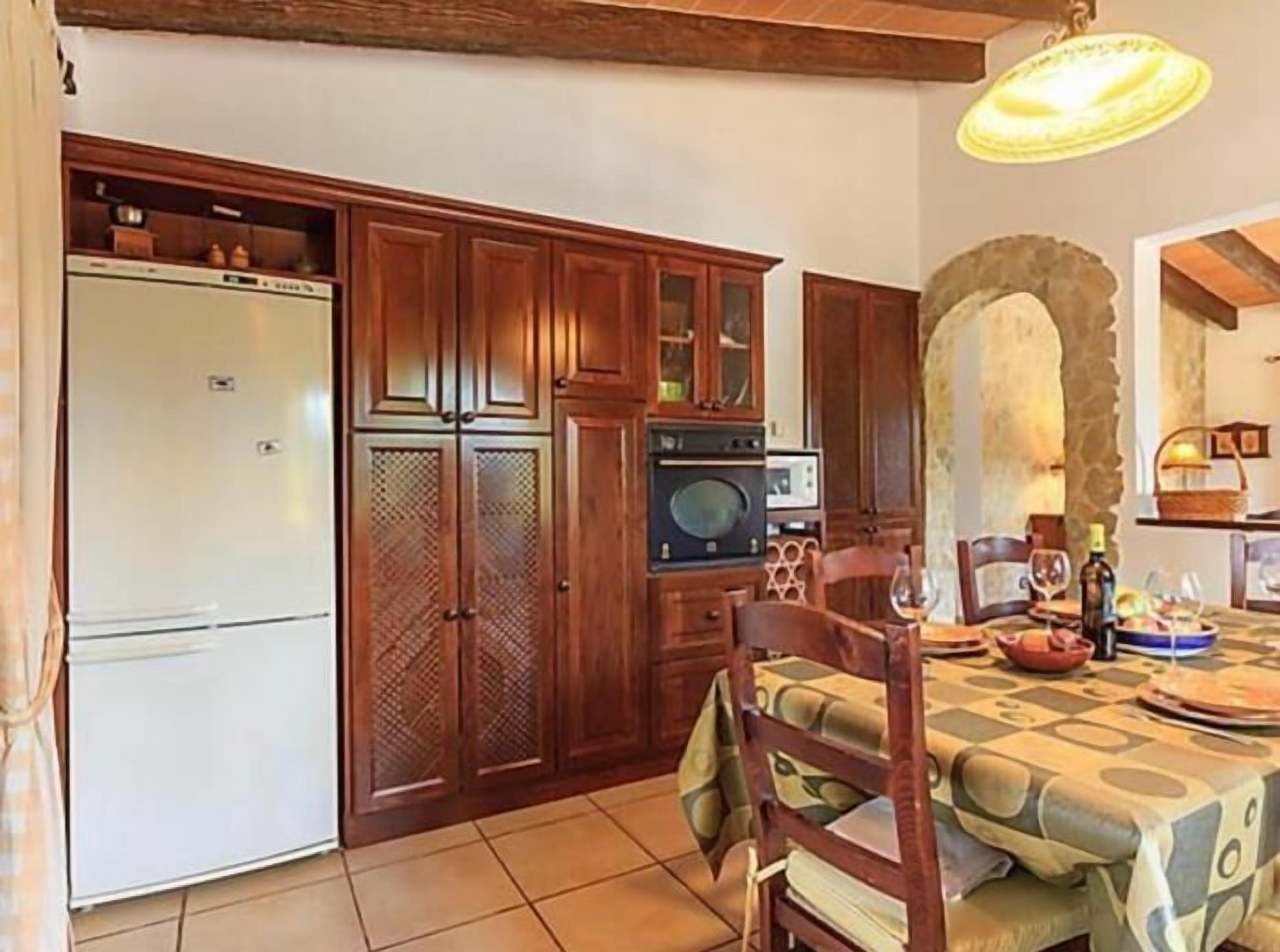 A kitchen with wooden cabinets, a refrigerator, an oven, and a dining table set with plates and glasses.