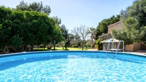 Una piscina con borde de piedra, rodeada de árboles y un edificio.