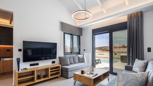 A modern living room with a flat-screen TV, wooden entertainment unit, grey sofa, and a coffee table. - Villa Vacasa - A Heaven of Luxury in the Heart of Crete (Aggeliana)
