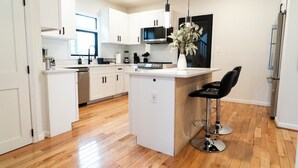 A modern kitchen with white cabinets, a central island with a black chair, and a stainless steel refrigerator. - Spacious 7-bedroom,  5 Full bathroom house. Walkers Paradise No car required! (Arlington)