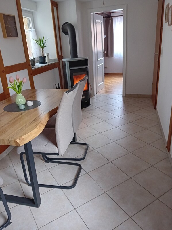 A dining area with a wooden table and a chair, a small plant on the table, and a fireplace in the background. - Cozy apartment in an old farmhouse (Zülpich)