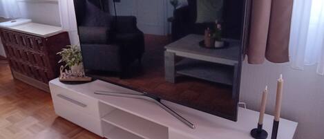 Et fladskærms-tv på et hvidt tv-møbel med en plante og stearinlys.