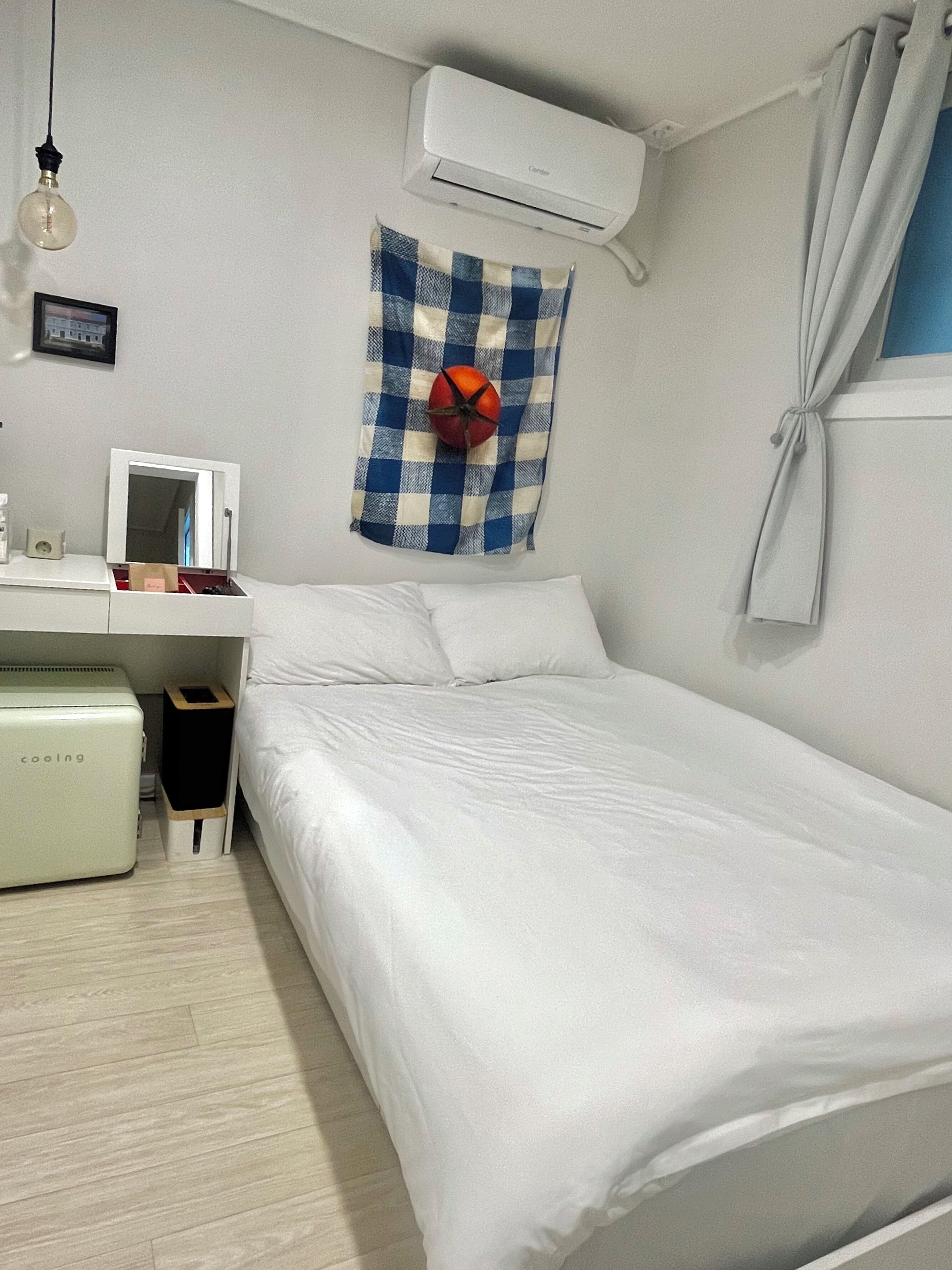 A bedroom with a bed, a desk with a computer, an air conditioner, and a wall-mounted heater.
