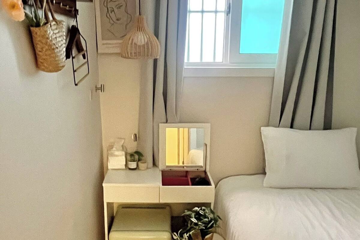 A bedroom with a bed, a bedside table, a mirror, and a window with curtains.