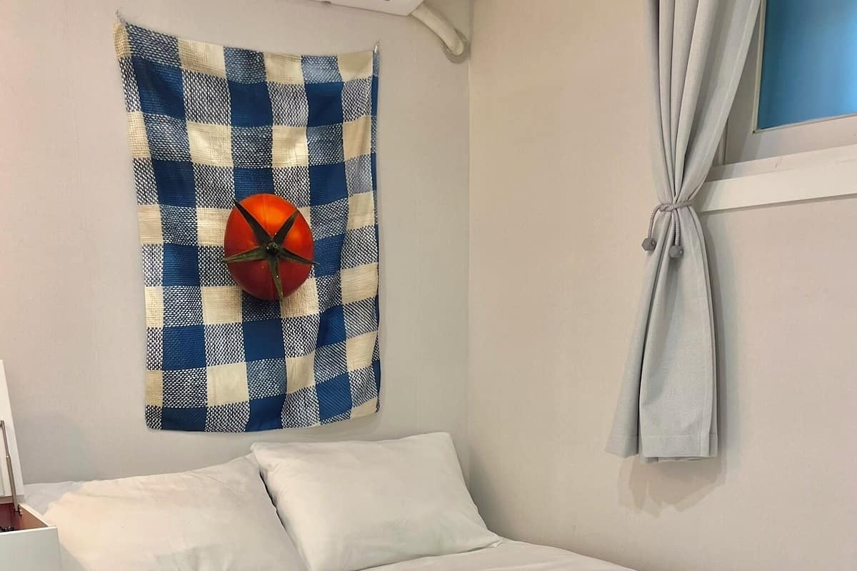 A neatly made bed with white linens, a checkered wall hanging above it, and a striped rug at the foot of the bed.