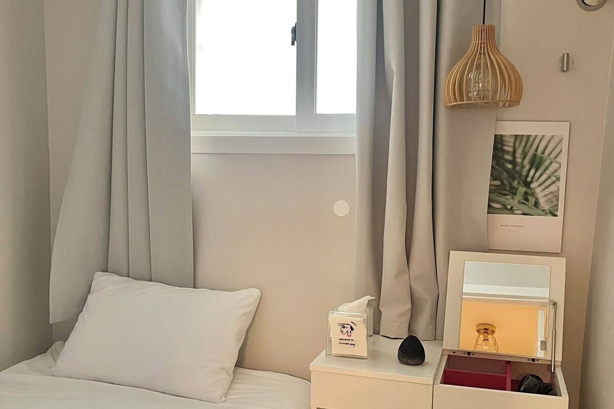 A bedroom with a bed, a nightstand, a small table, a lamp, and a window with curtains.