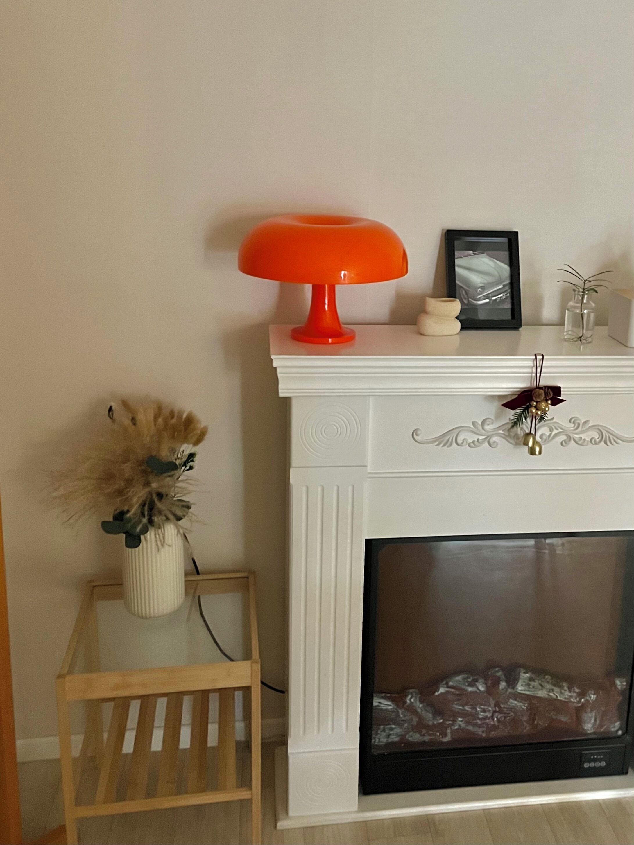 Una chimenea blanca con una lámpara de mesa roja, un cuadro enmarcado y objetos decorativos en la repisa.