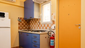 A compact kitchen with a white refrigerator, blue cabinets, a gas stove, and a window above the sink. - Studio House da Pasolini a Mastroianni (Rome)