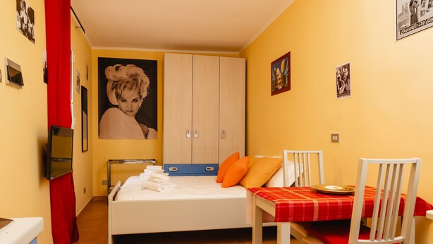 A bedroom with a bed, a table with chairs, a wardrobe, and a poster on the wall. - Studio House da Pasolini a Mastroianni (Rome)
