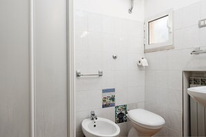 A bathroom with a toilet, bidet, and a small window.
