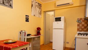 A compact kitchen with a refrigerator, stove, and a small dining table with a red tablecloth. - Studio House da Pasolini a Mastroianni (Rome)