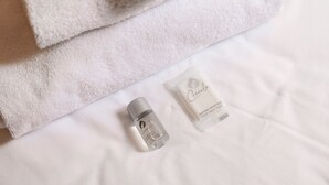 A neatly folded white towel, a small bottle of soap, and a sachet of soap on a white bed. - Studio House da Pasolini a Mastroianni (Rome)