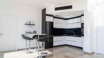 Una cucina moderna con mobili bianchi, un piano di lavoro nero e un forno integrato. Ci sono due sgabelli da bar e un piccolo tavolo con un vaso.