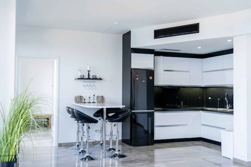 Una cucina moderna con mobili bianchi, un frigorifero nero e un bancone con sgabelli.