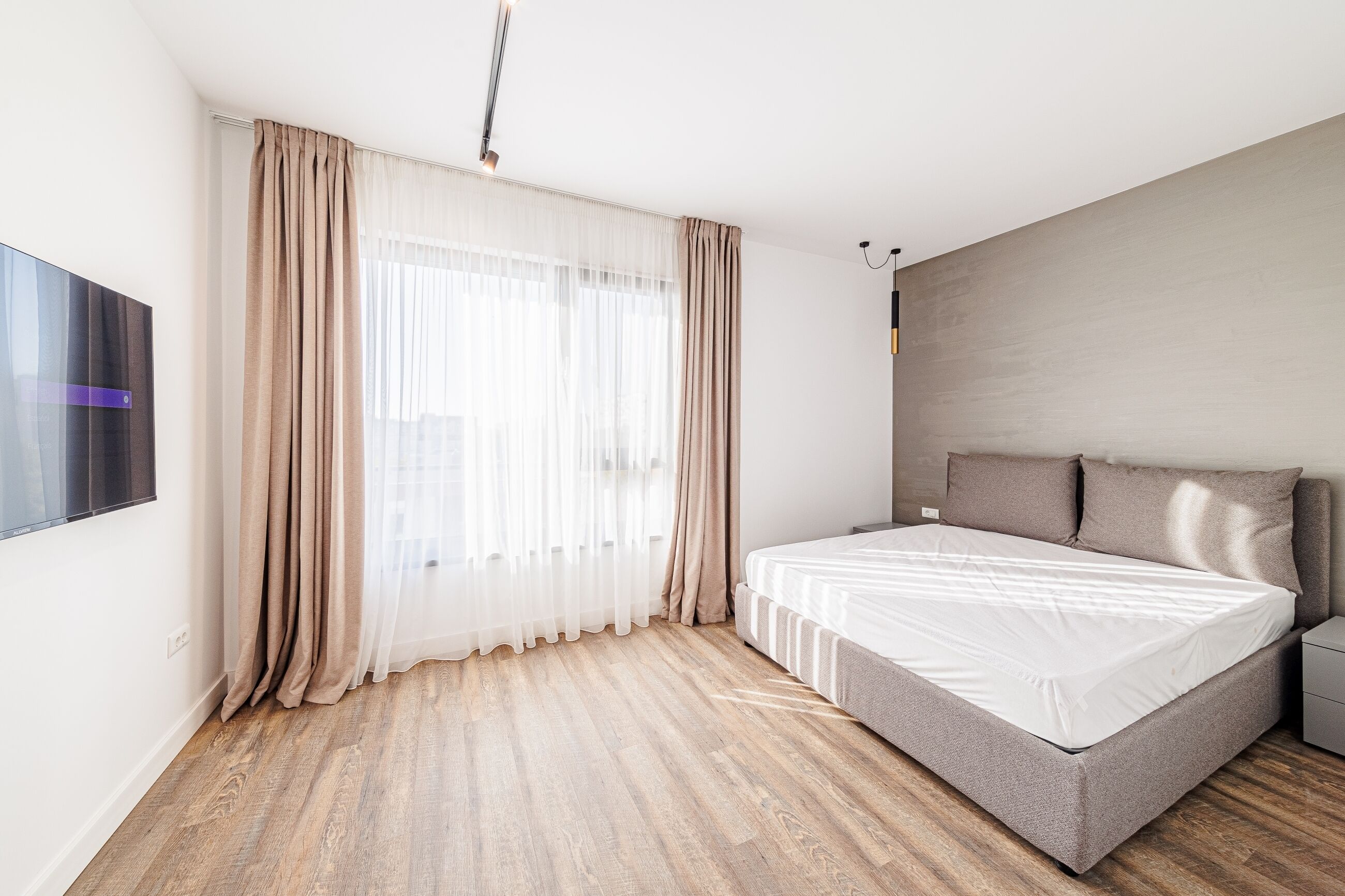 Un dormitorio moderno con una cama grande, un televisor de pantalla plana y una ventana con cortinas translúcidas.
