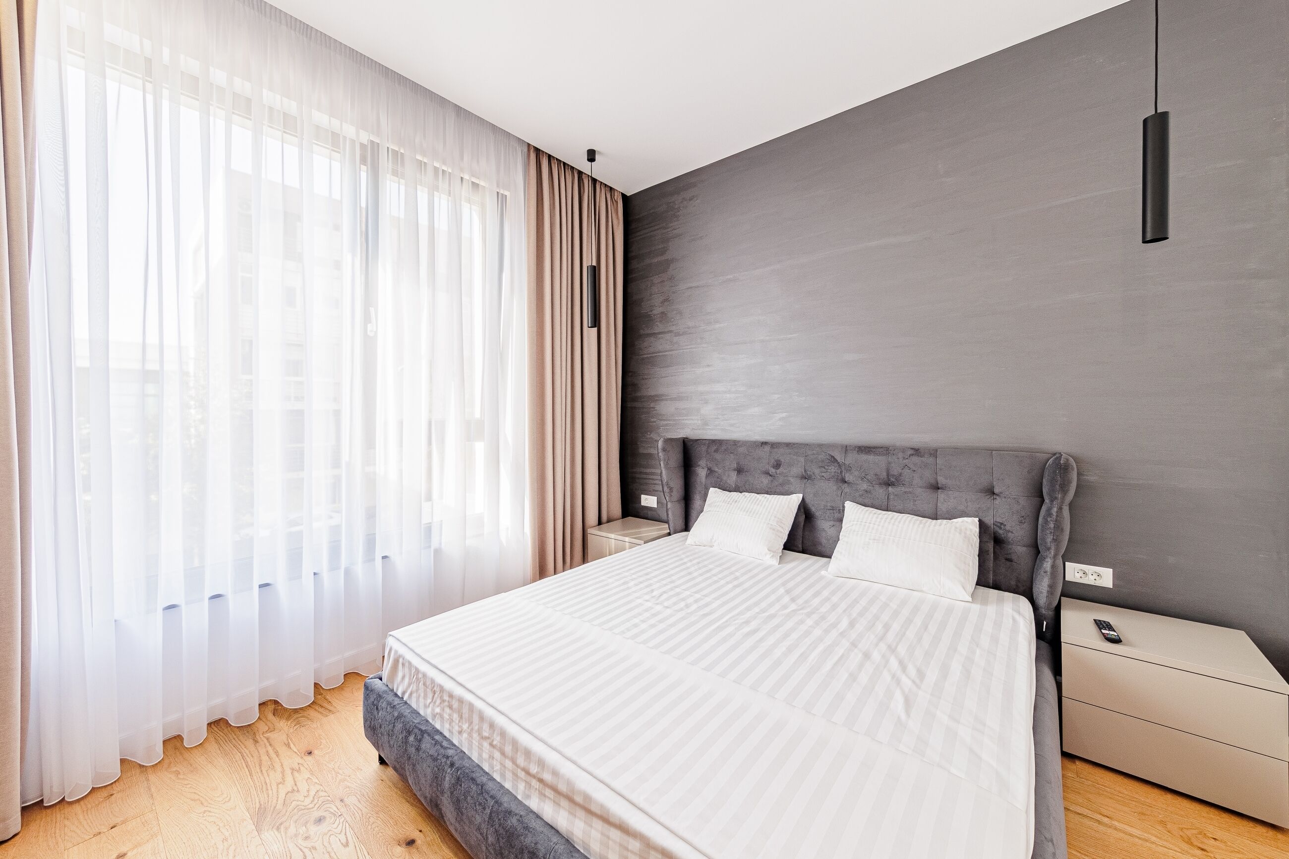 Quarto moderno com uma cama grande, uma mesinha de cabeceira e um candeeiro suspenso.