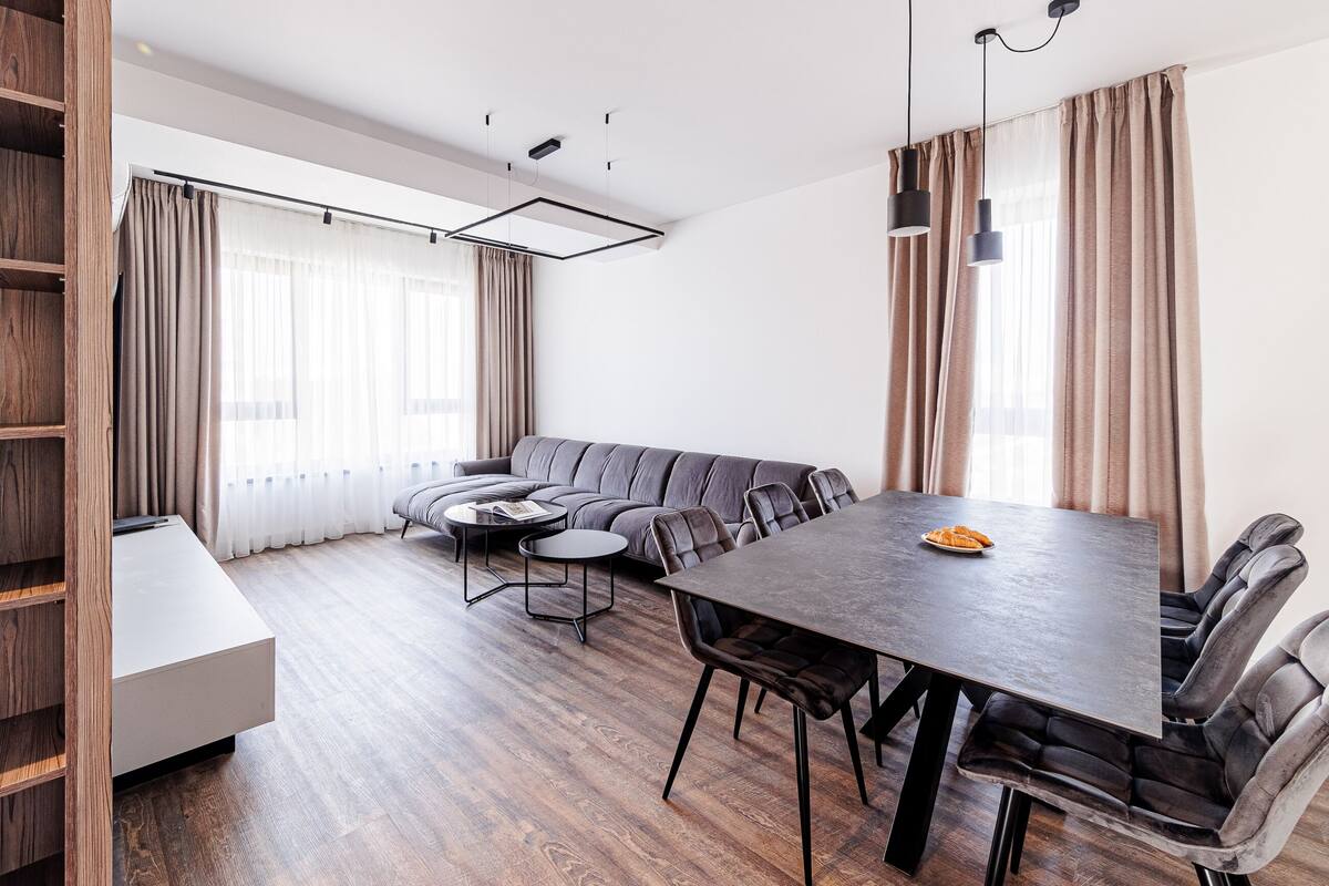A modern living room with a sofa, a dining table with chairs, a coffee table, and a bookshelf.