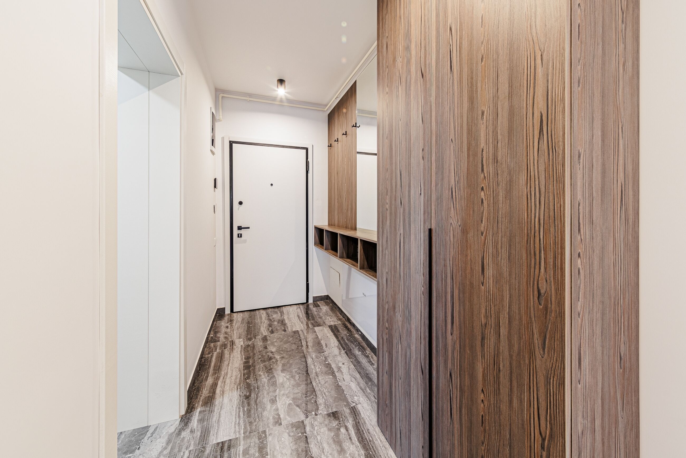 Un pasillo con pared de paneles de madera, una puerta blanca y piso de mármol.