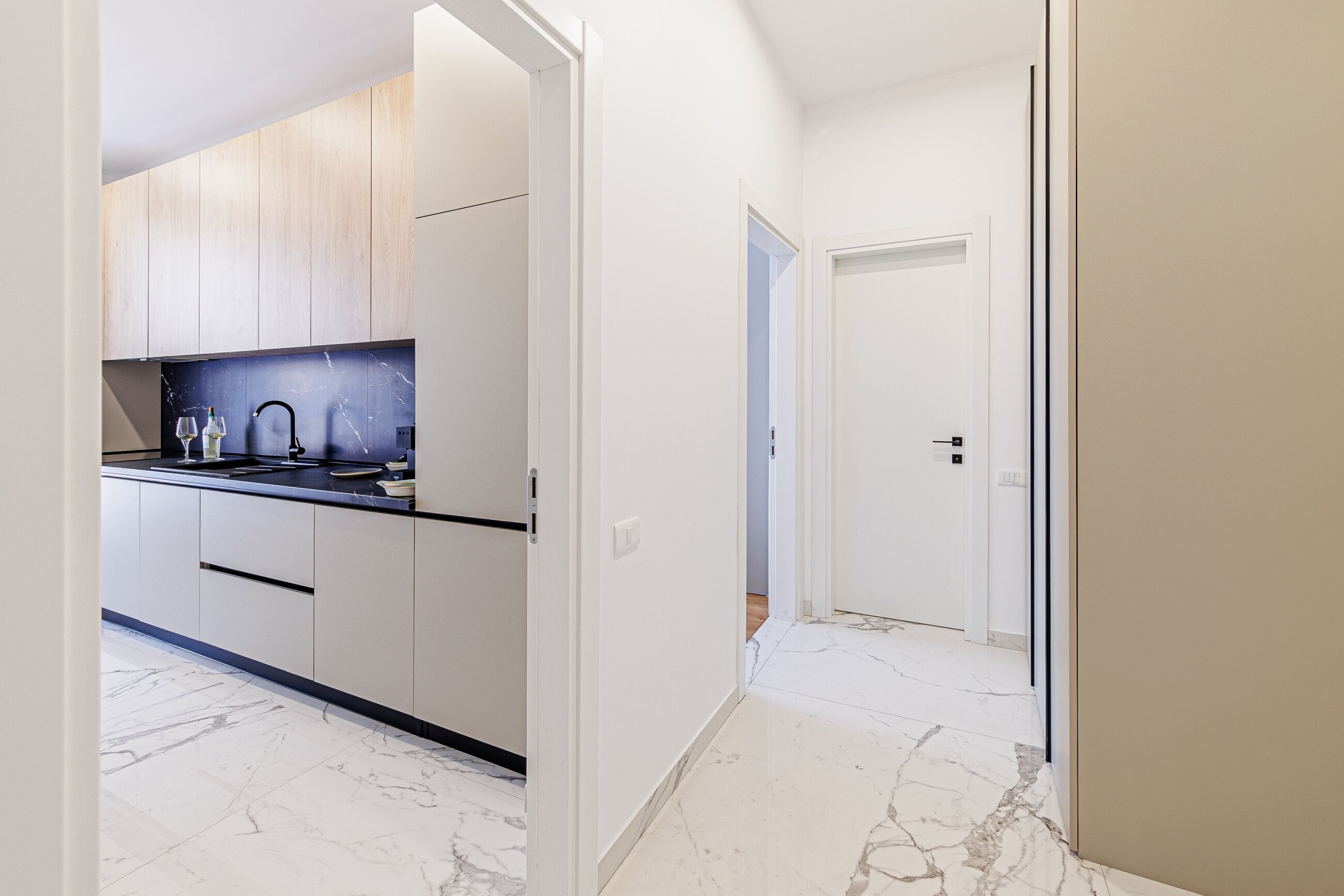 A modern kitchen with white cabinets, a black countertop, and a marble backsplash.