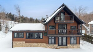 A two-story log cabin with a balcony, large windows, and a stone foundation. - Escape to Grandes-Piles (Grandes-Piles)