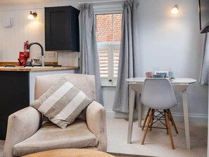 A cozy living area with a sofa, a dining table with chairs, a kitchen area, and a window with curtains.