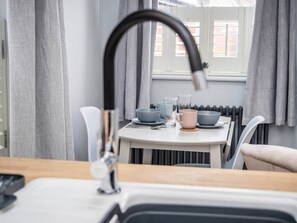 A kitchen with a modern faucet, a dining table with bowls and cups, and a window with curtains.