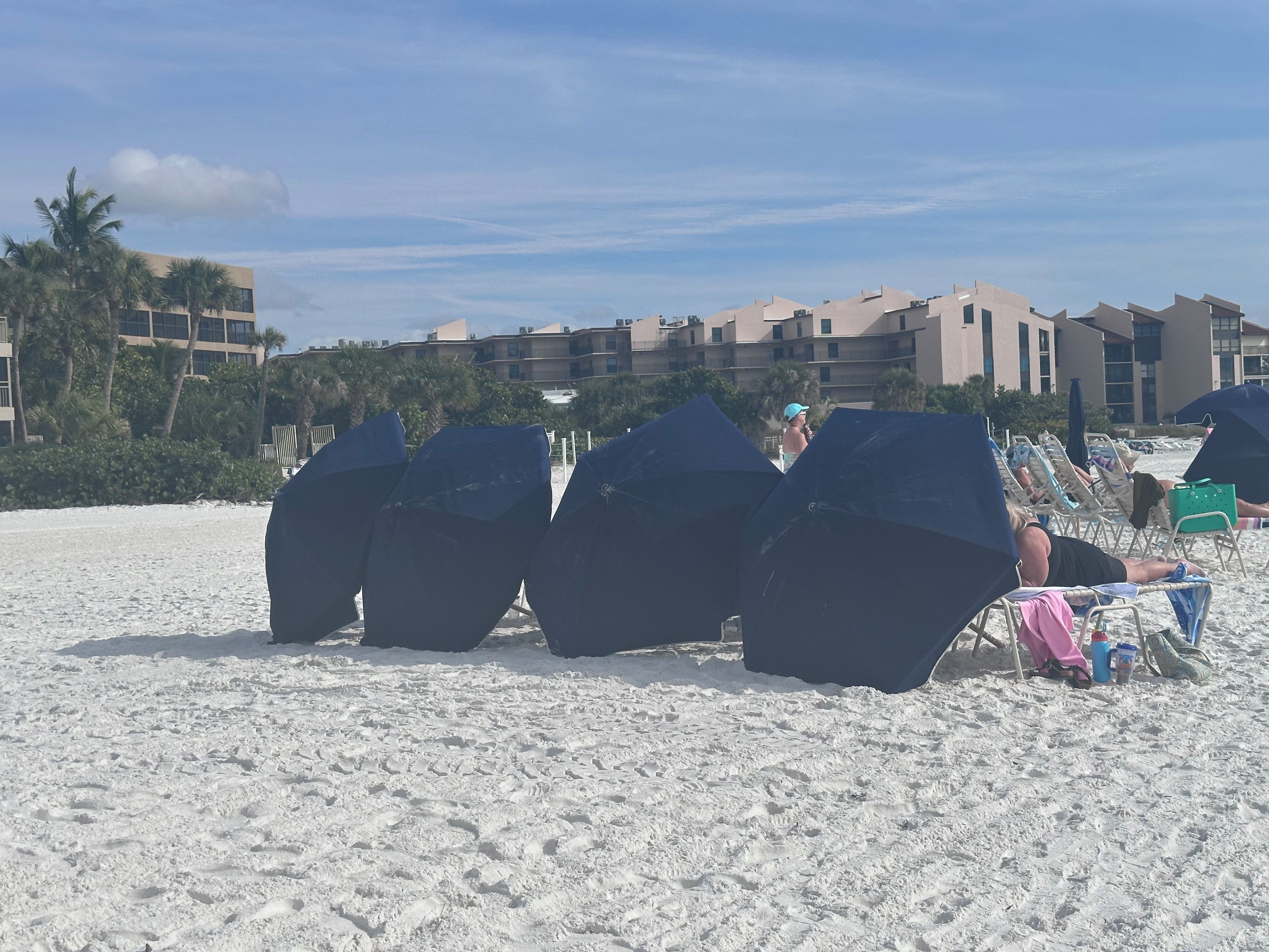 A beach with umbrellas, lounge chairs, and a building in the background.