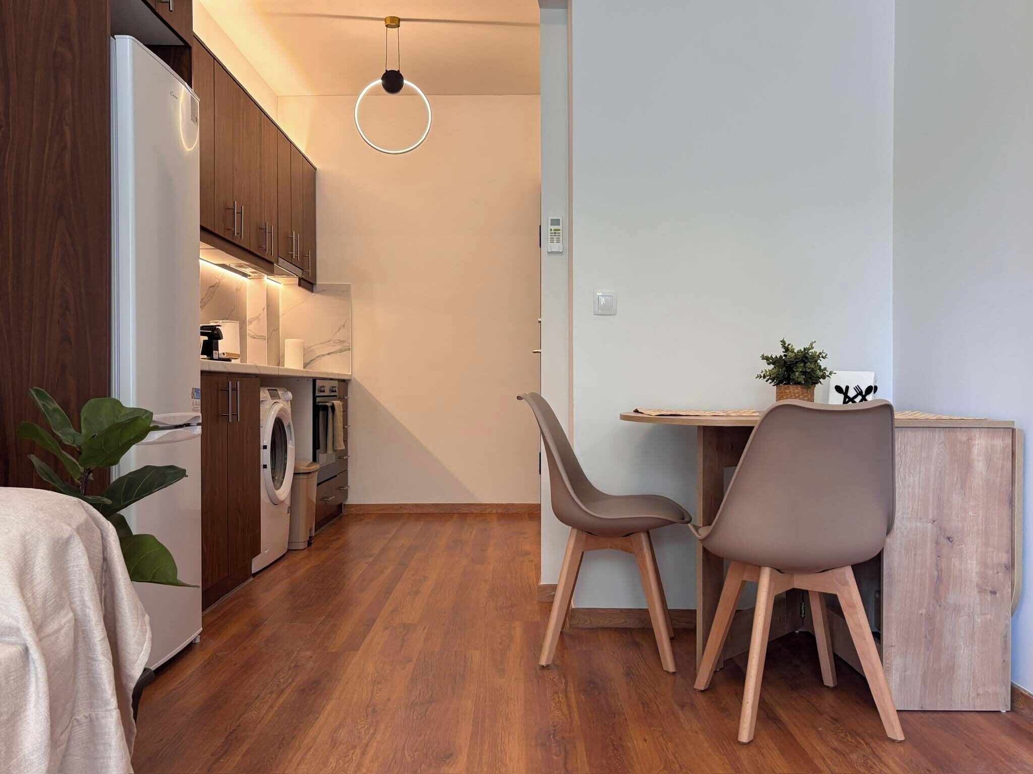A compact kitchen with modern appliances, a dining area with two chairs, and a wooden floor.