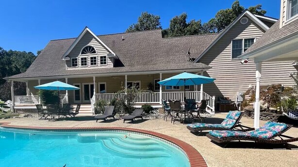 A swimming pool with a brick edge, surrounded by lounge chairs and umbrellas. - Beautiful Kent Island Getaway with Pool (Stevensville)