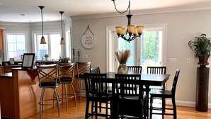 A spacious kitchen with wooden flooring, a dining area with a chandelier, and large windows providing natural light. - Beautiful Kent Island Getaway with Pool (Stevensville)