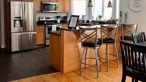 A modern kitchen with wooden cabinets, stainless steel appliances, a central island with bar stools, and pendant lighting. - Beautiful Kent Island Getaway with Pool (Stevensville)