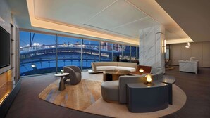 Una habitación de hotel moderna con un ventanal que ofrece vistas a la ciudad, un sofá, una mesita de centro y una pequeña mesita auxiliar.