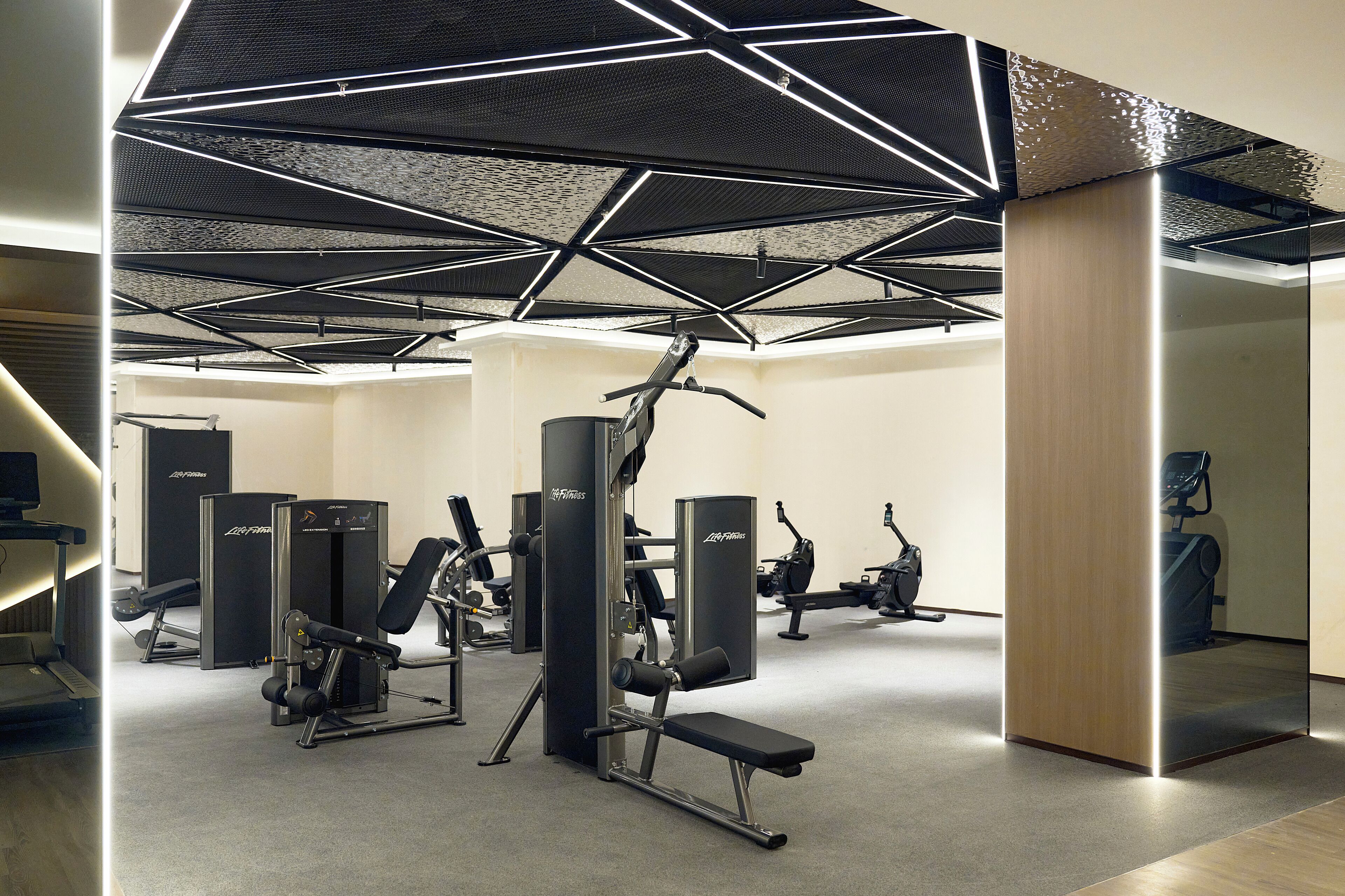 Un gimnasio con equipo de ejercicio diverso, un espejo grande y un diseño geométrico en el techo.