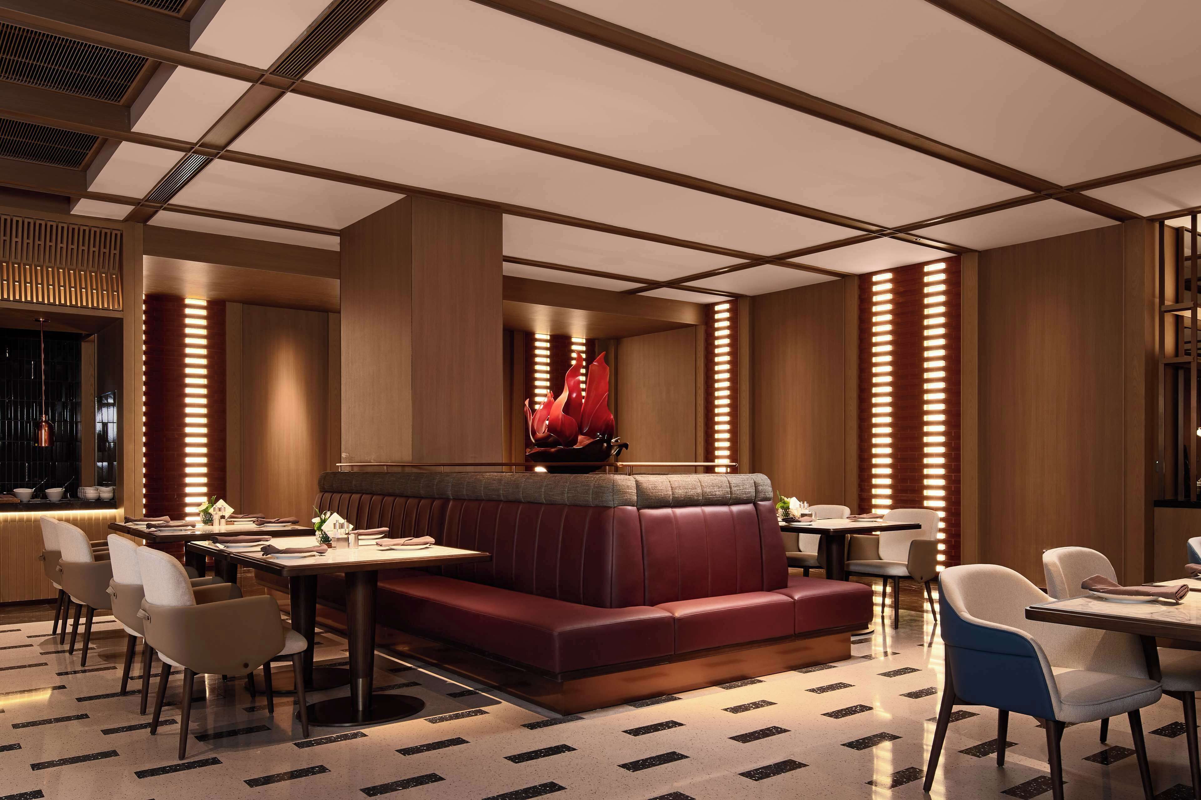 A modern restaurant with a central red booth, white and blue chairs, and a patterned floor.