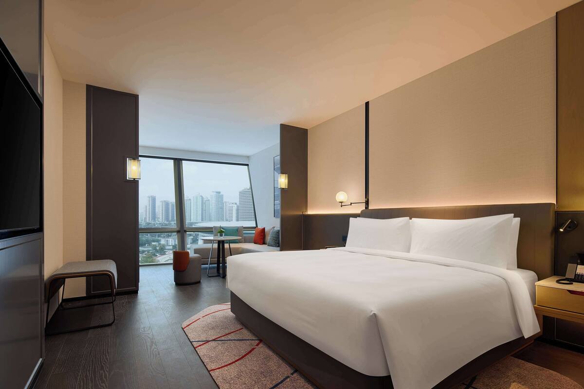 Habitación de hotel moderna con una cama grande, un escritorio y vistas a la silueta urbana.