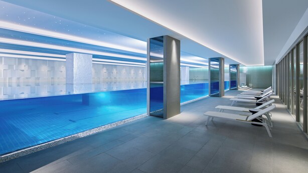 Una piscina interior moderna con agua cristalina, sillas de descanso y una pared de vidrio que ofrece vistas a la piscina.