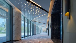 Un pasillo moderno con puertas de cristal, una columna de mármol, suelo estampado e iluminación de techo geométrica.