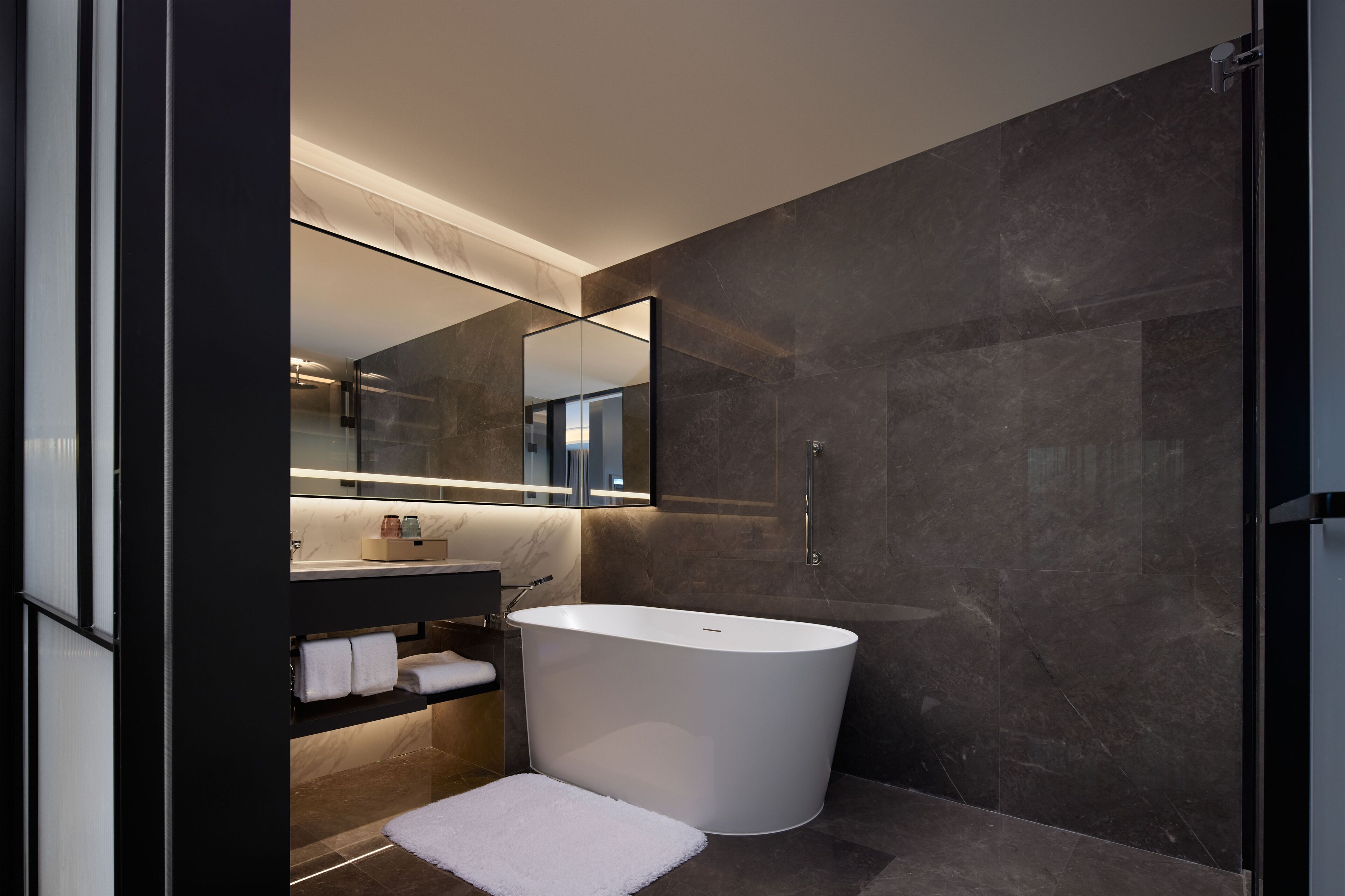 A modern bathroom with a freestanding bathtub, a glass shower enclosure, and a marble-tiled wall.