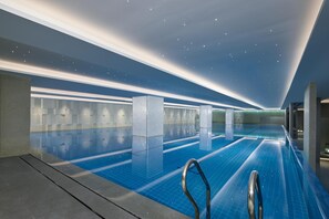 A modern indoor swimming pool with clear blue tiles, a metal handrail, and a ceiling with embedded lights. - Radisson Blu Hotel, Shanghai Stadium (Shanghai)