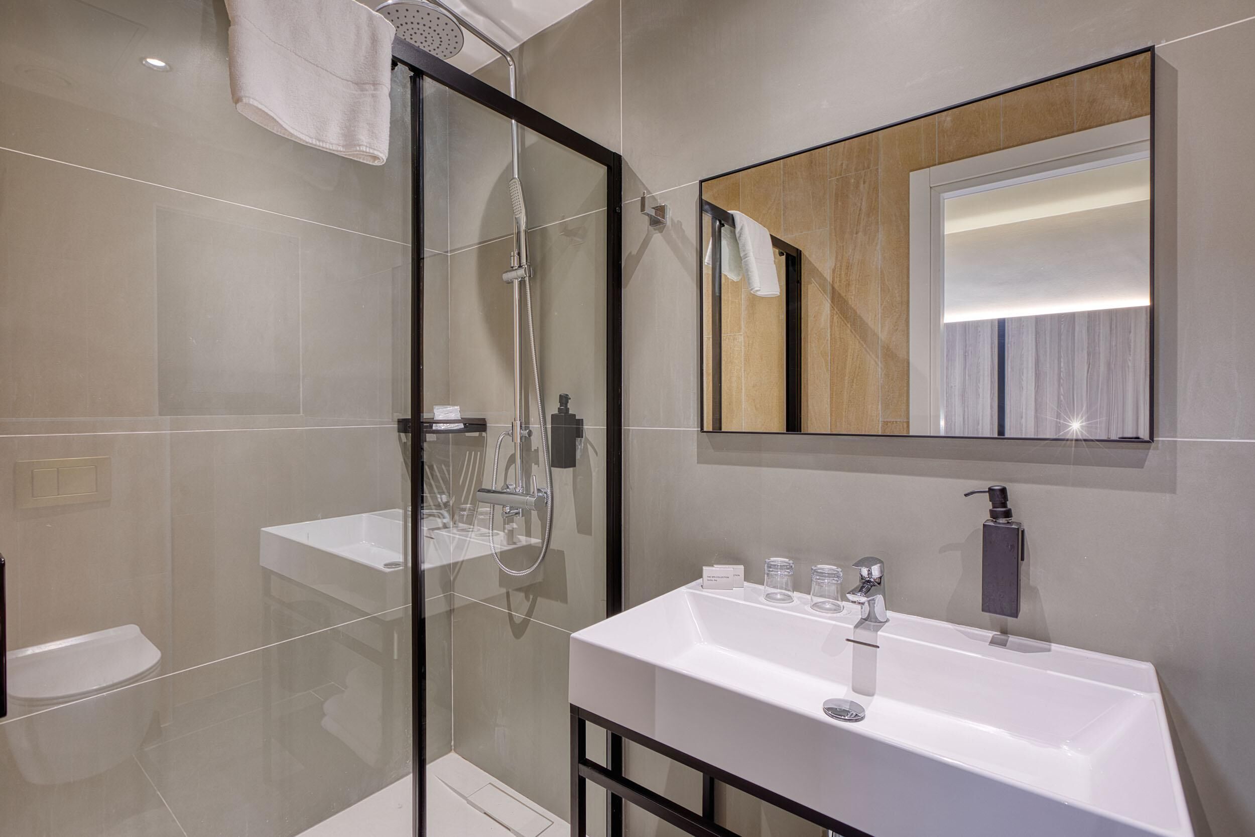 A modern bathroom with a glass-enclosed shower, a white sink, and a mirror with a wooden frame.
