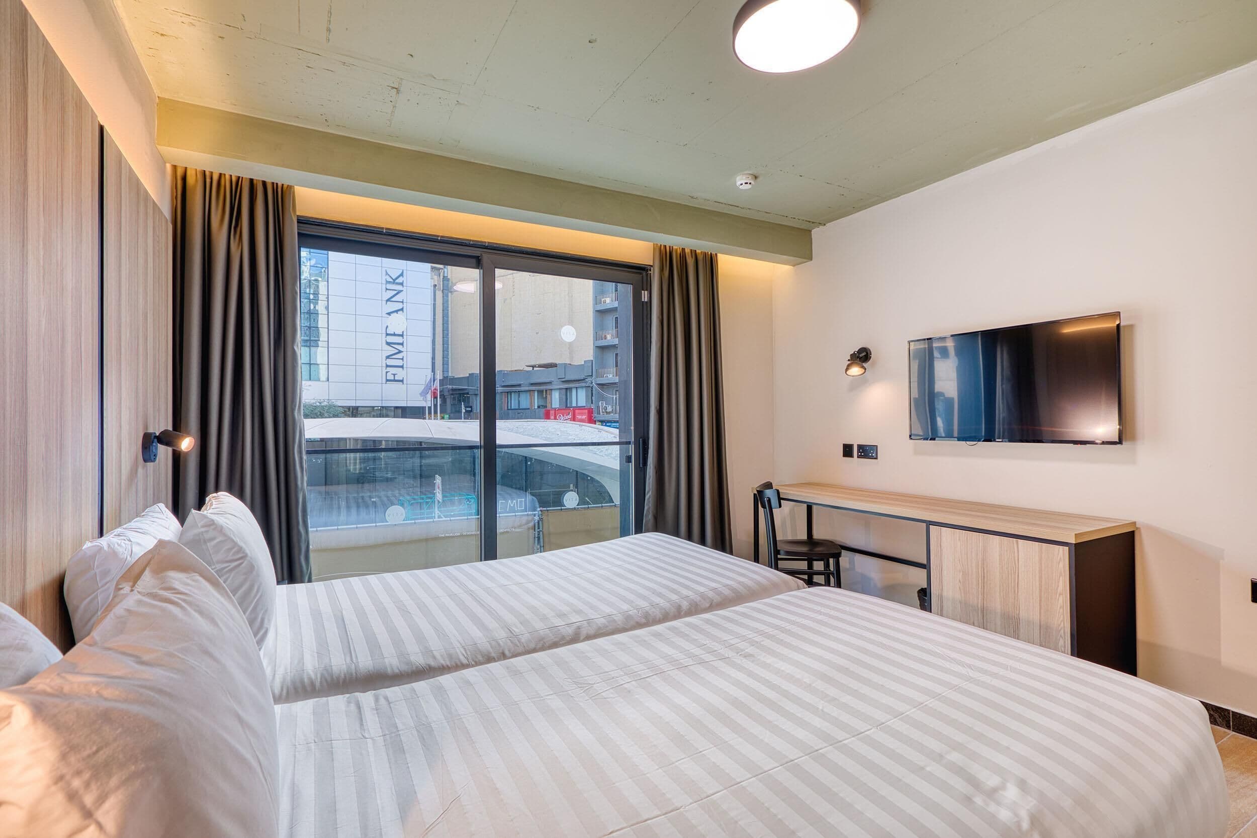 Habitación de hotel con cama, escritorio, silla, televisor y vista al exterior.